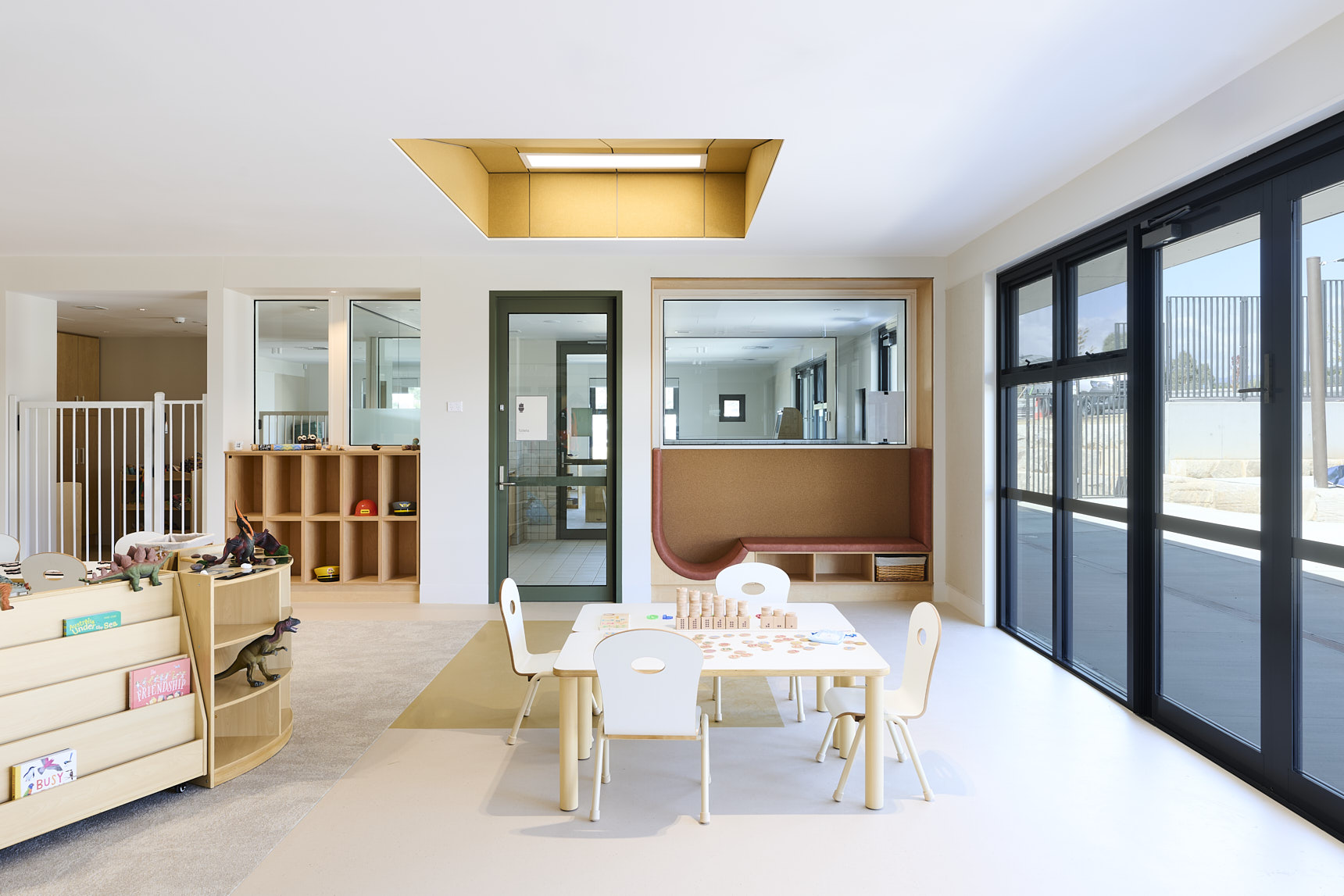 Modern early‑learning classroom with a small white table, child‑sized chairs, wooden blocks, toy dinosaurs, and curved shelving. Features cubby storage, a built‑in seating nook, and natural light for a calm, organised preschool environment.