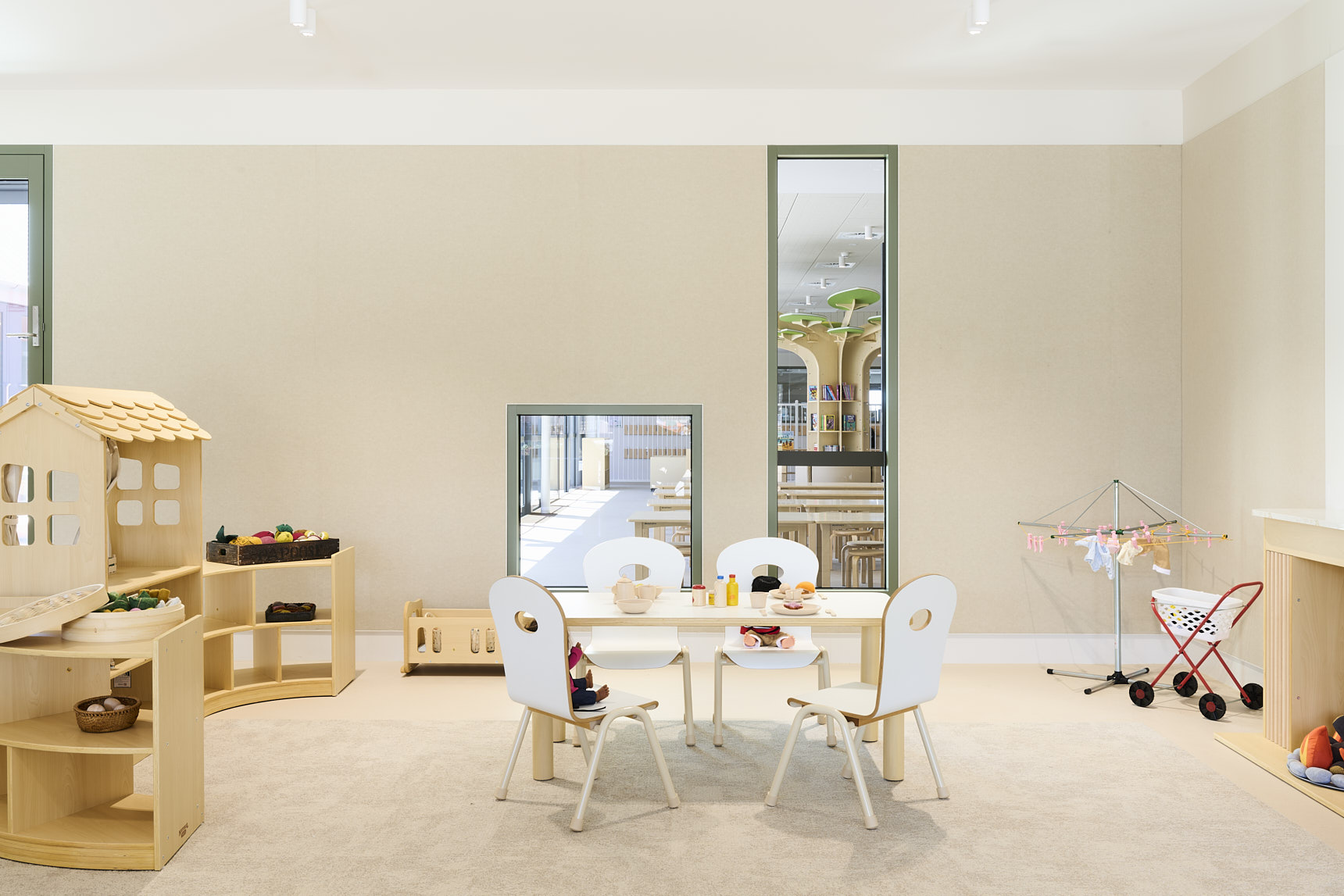 Children’s dramatic playroom featuring a toy kitchen setup with pretend food, a wooden playhouse shelf, doll bed, toy clothes drying rack, and stroller. Bright, organised space designed to support imaginative play in early‑learning settings.